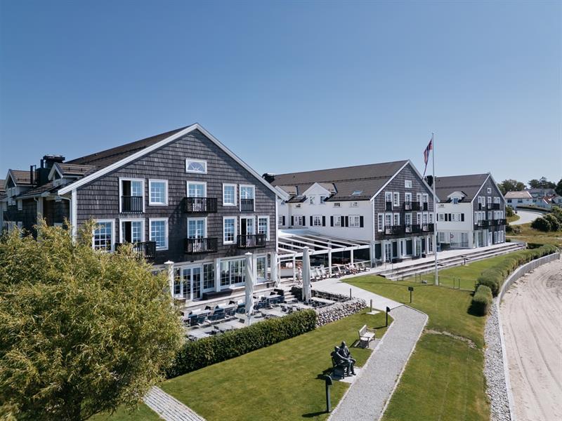 Fasade Støtvig Hotell i tre og hvite vinduer. Strand i forgrunn