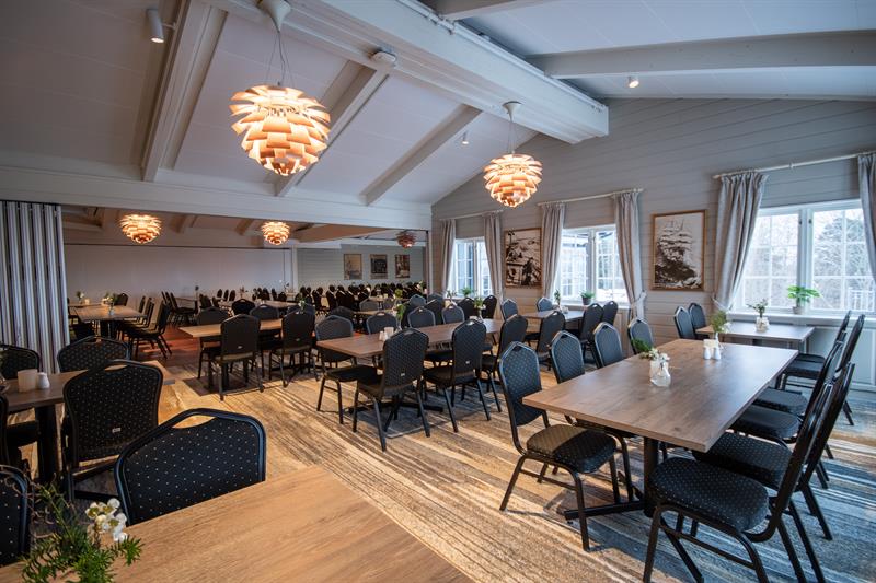Restaurant with many chairs and tables. Light painted walls and tilted ceilings.