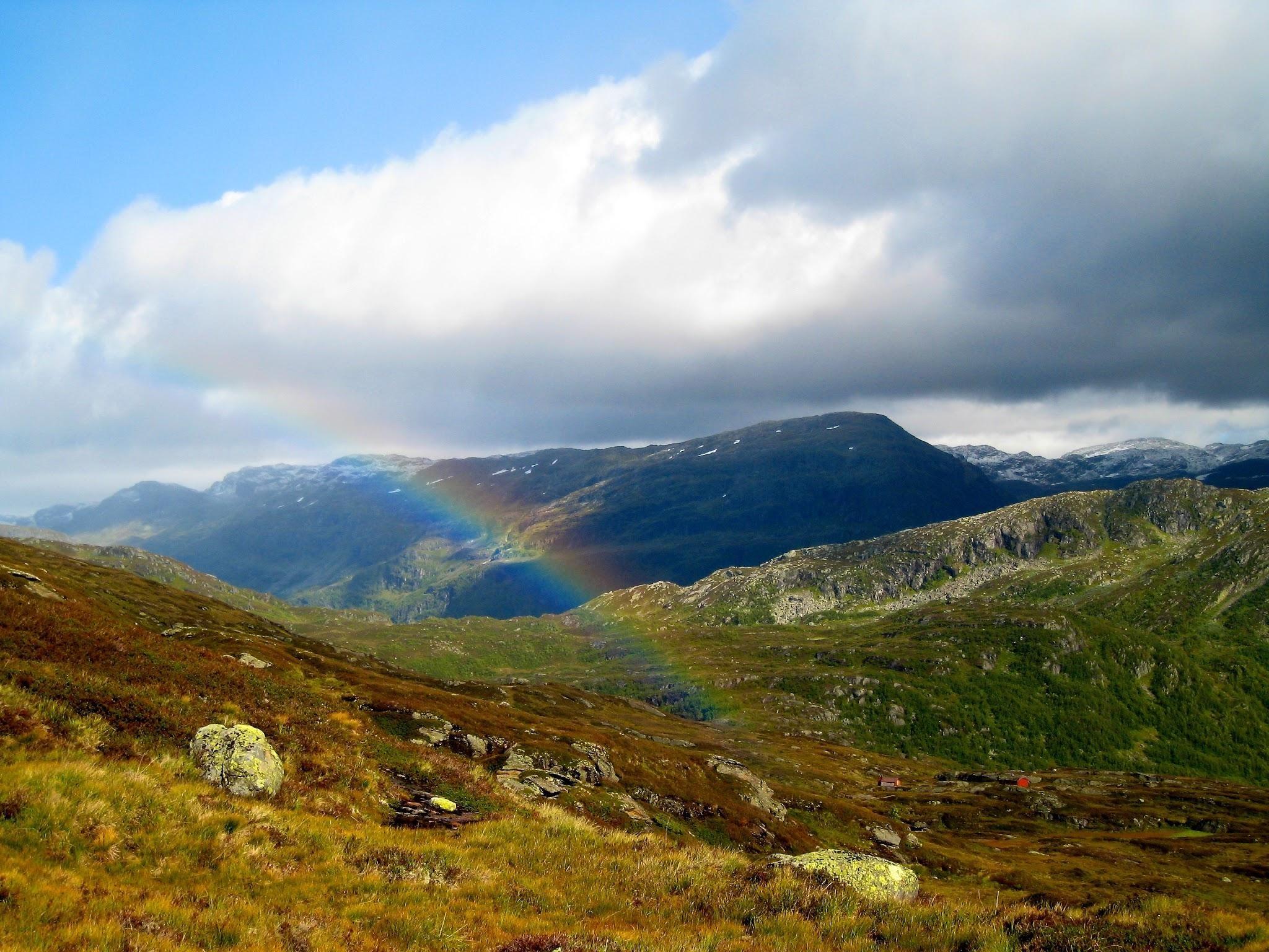A view over several mountains with a rainbow in the middle of the picture 