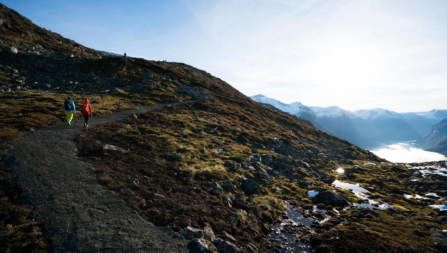 Hiker walking across the mountain landscape at Hoven, with the fjord and mountains stretching into the distance.