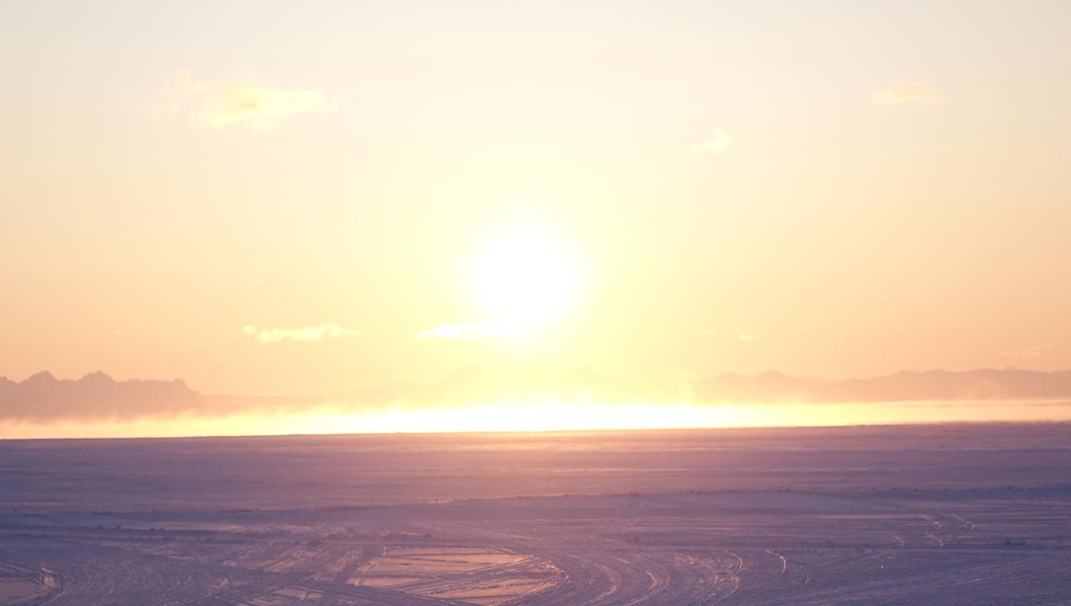 Midnattssola som skinner over en fjord og et snødekt landskap