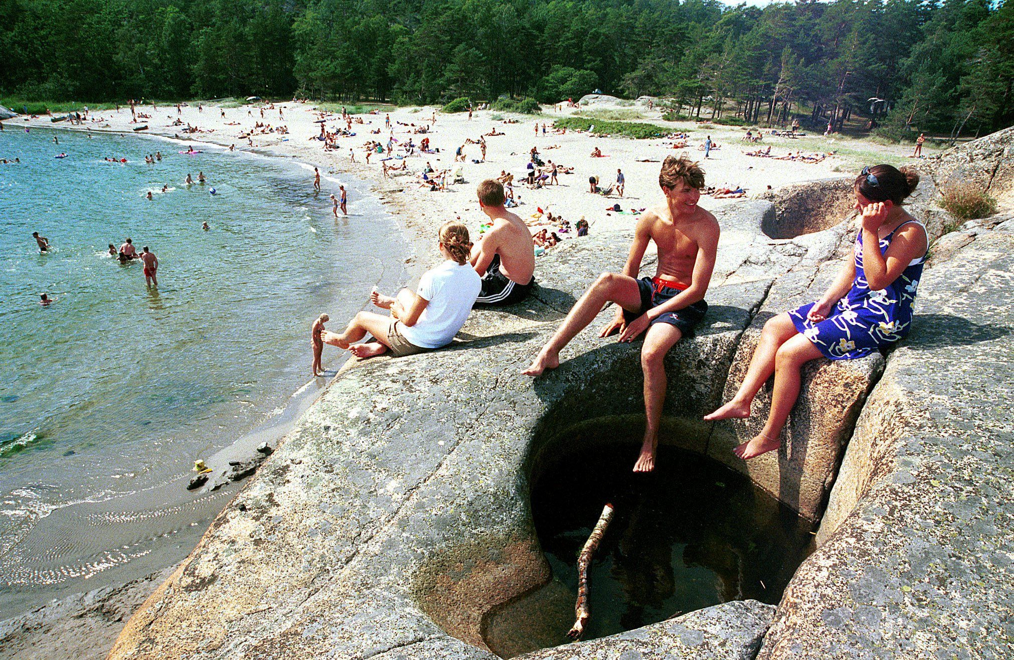 Barn på svaberg og mange mennesker på sandstrand