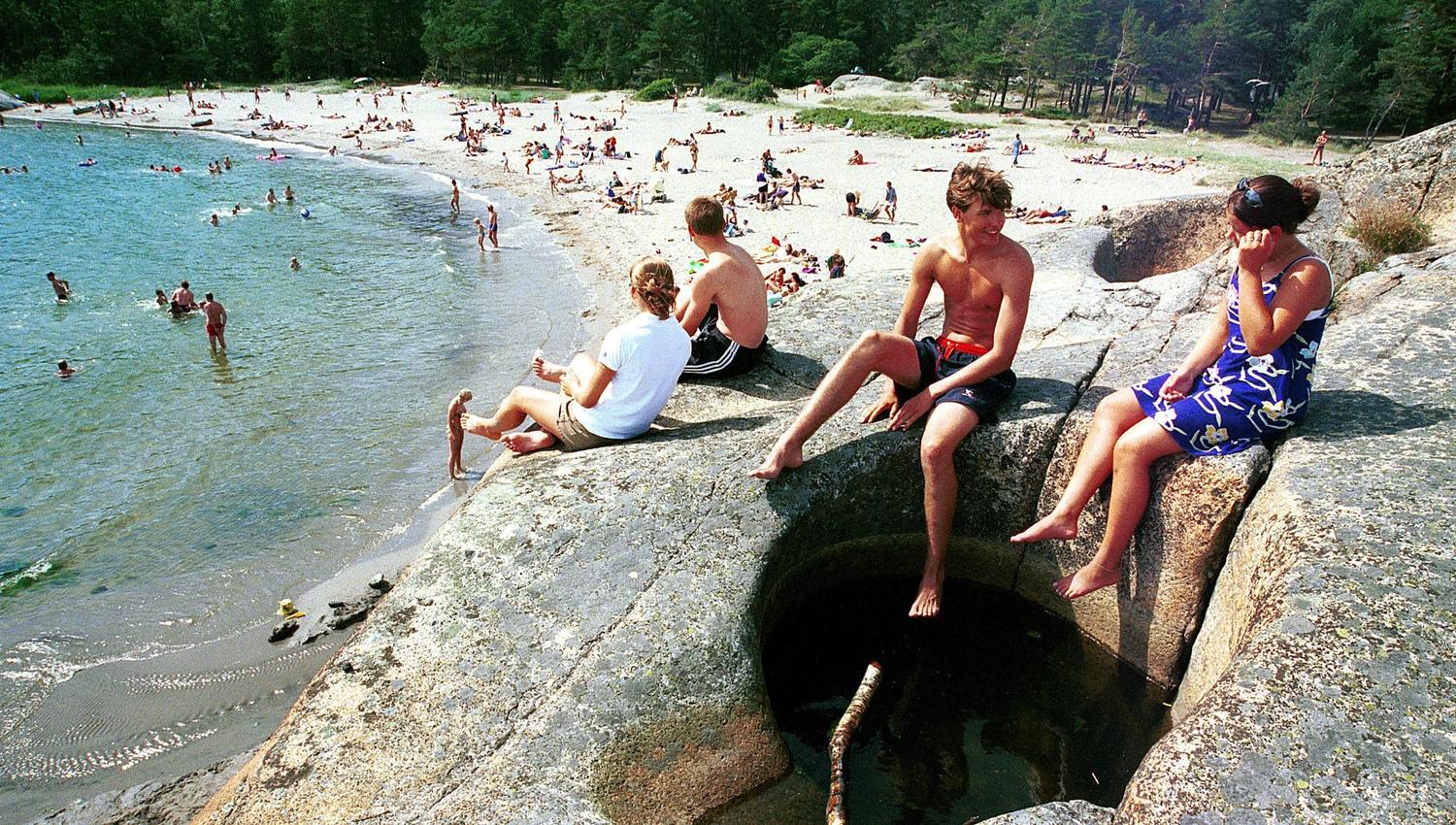 Barn på svaberg og mange mennesker på sandstrand