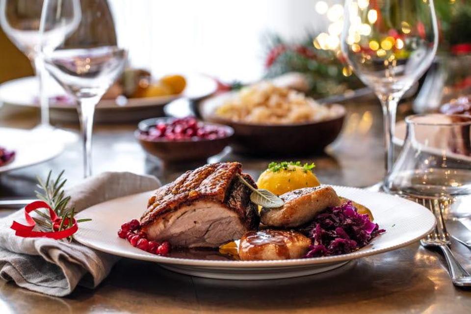 Bildet viser et pent dekket bord med en tallerken mat. På tallerkenen ligger det ribbe, poteter, saus og rødkål. Det står vinglass og pynt med lys rundt, så det ser ut som et koselig julemåltid.