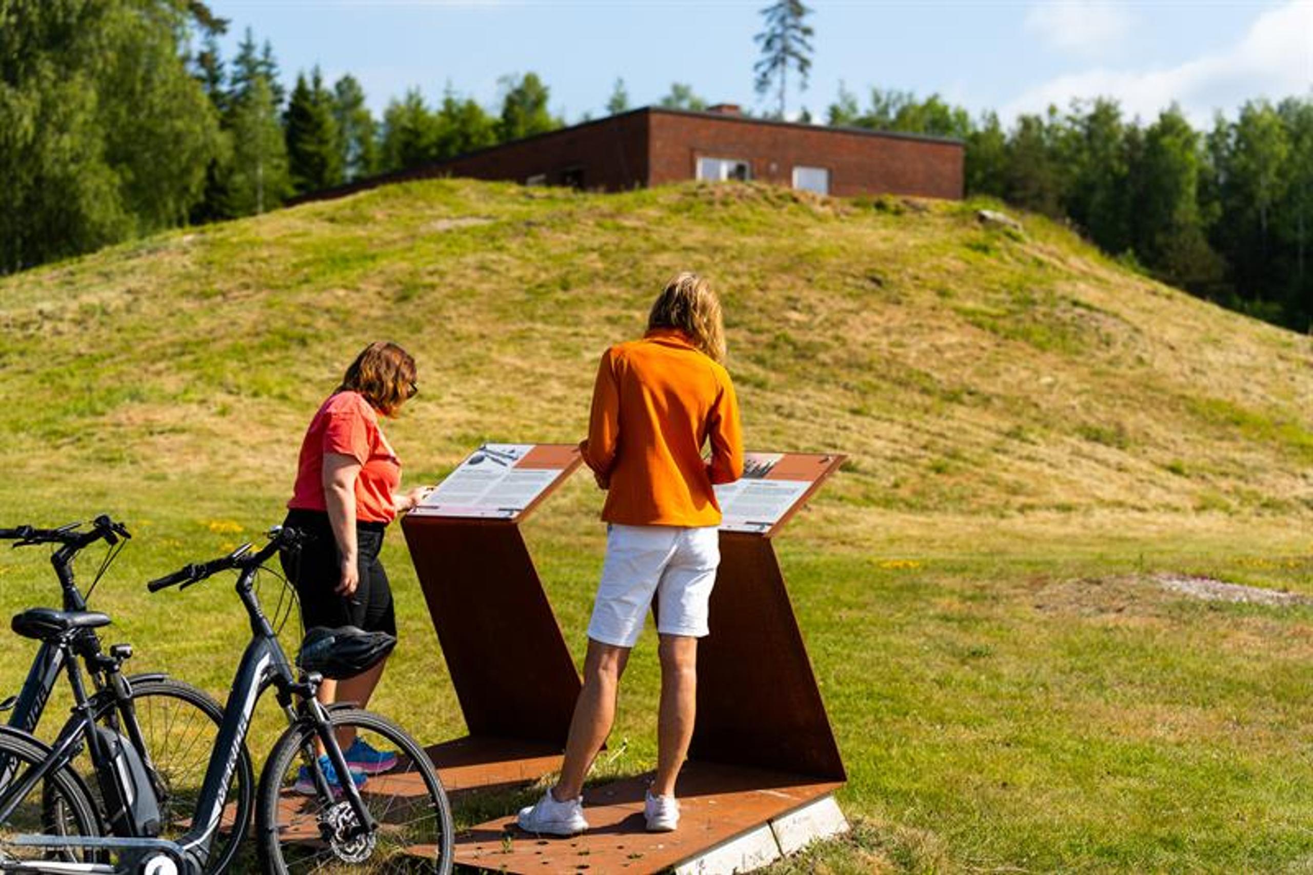 Syklister som leser på informasjon om historisk grunn, jernaldergravene.