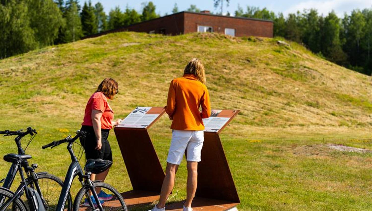 Syklister som leser på informasjon om historisk grunn, jernaldergravene.