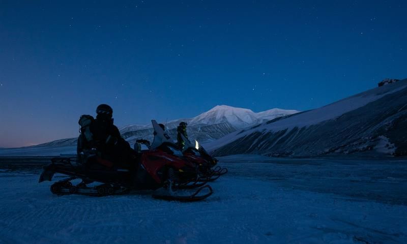 To snøscootere med sjåfører står på et snødekt landskap under polarnatten