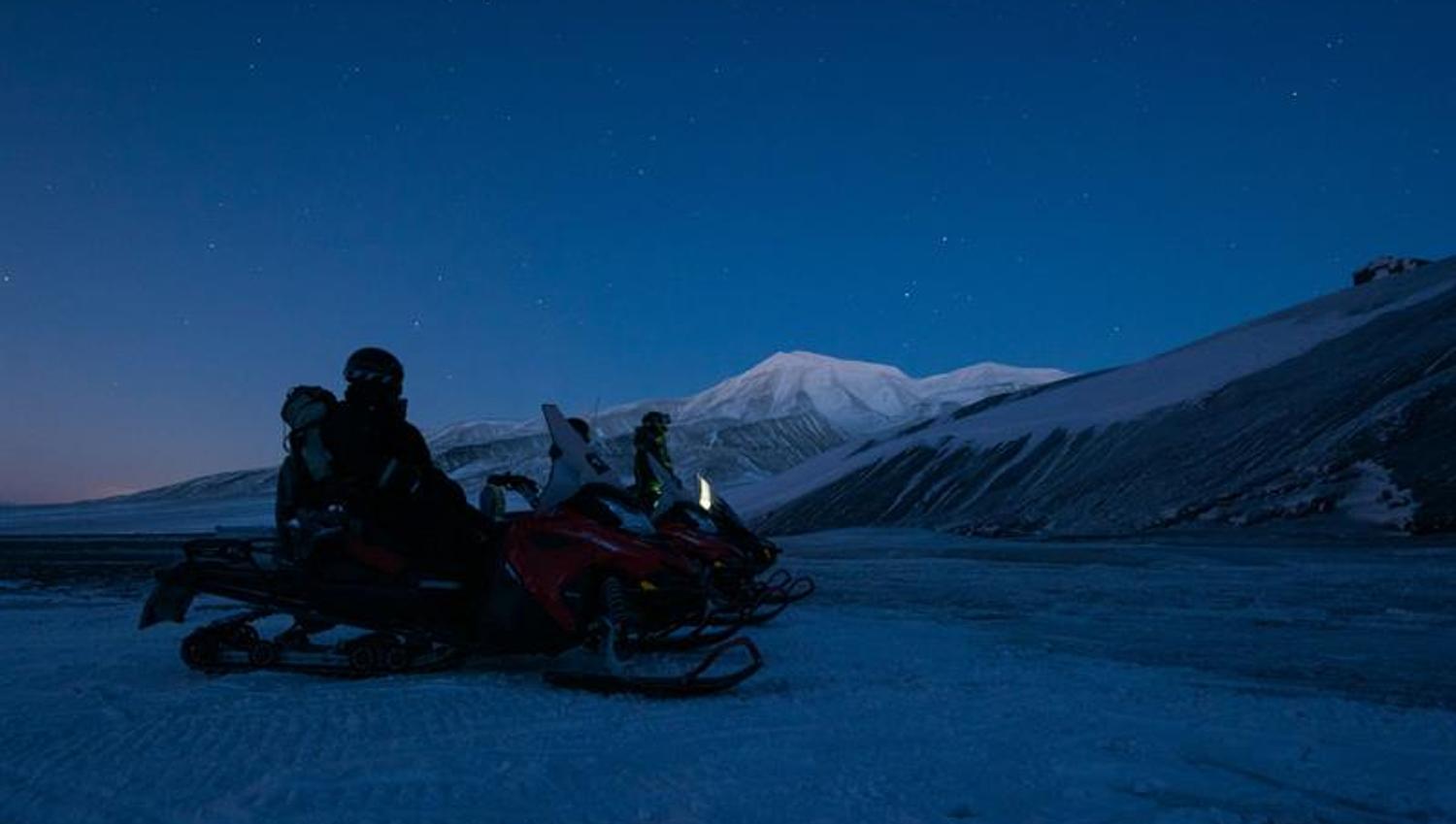 To snøscootere med sjåfører står på et snødekt landskap under polarnatten