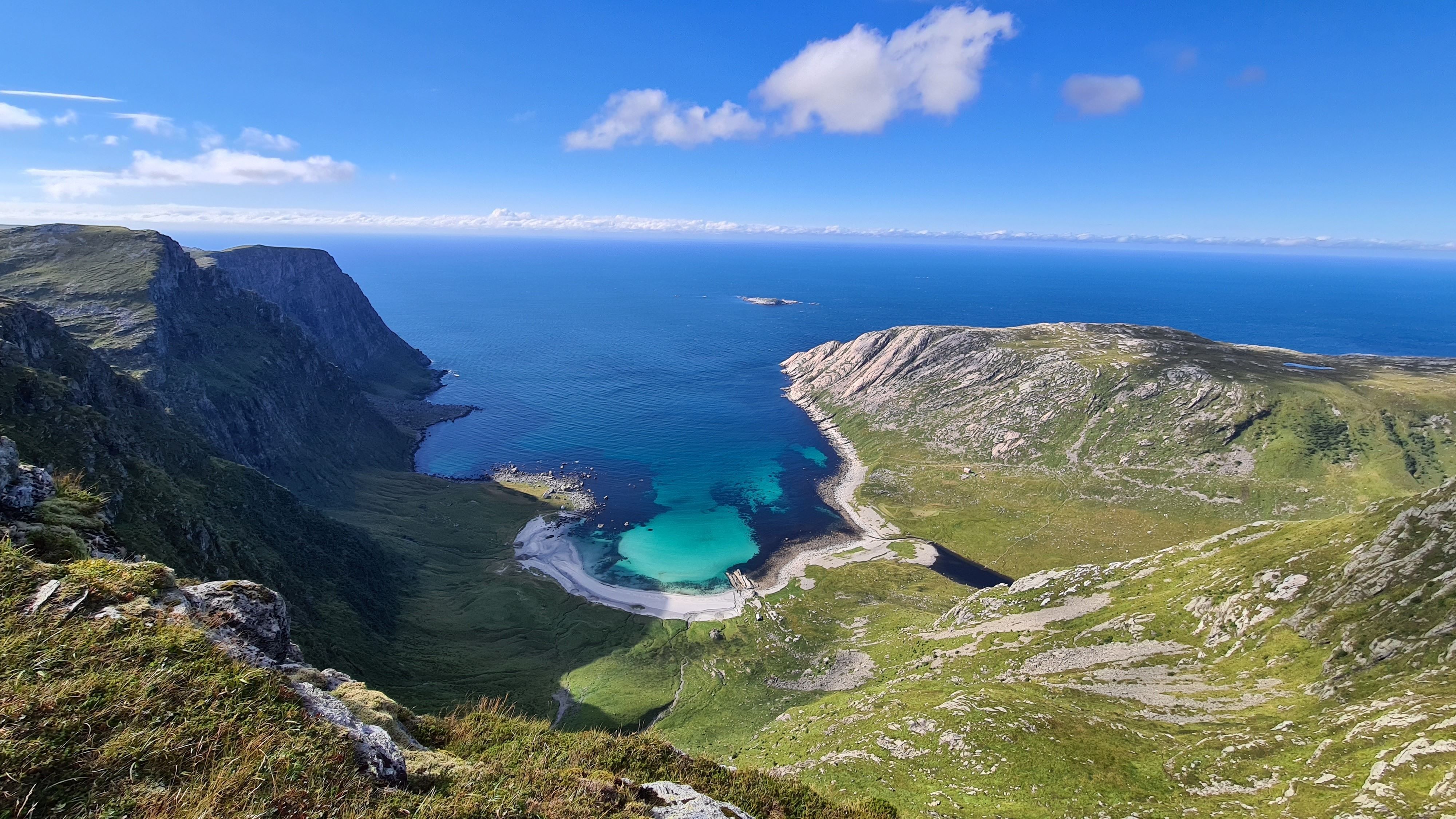 Opplevingar i nærleiken av Bremanger Fjordhotell: Utsikt frå fjell mot Vetvika, ei turkis strandvik, bratte klipper og ope hav under blå himmel med skyer..