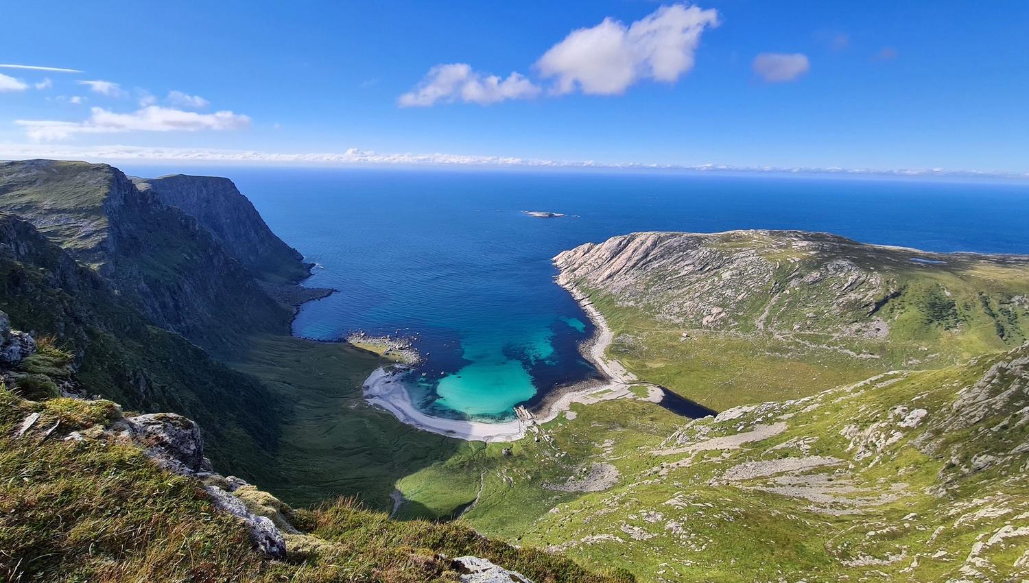 Opplevingar i nærleiken av Bremanger Fjordhotell: Utsikt frå fjell mot Vetvika, ei turkis strandvik, bratte klipper og ope hav under blå himmel med skyer..