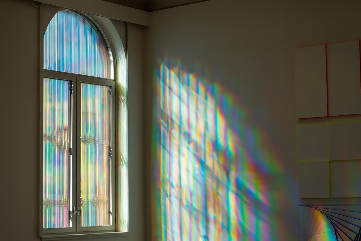 Rainbow‑colored light patterns projected on a wall and around a window.
