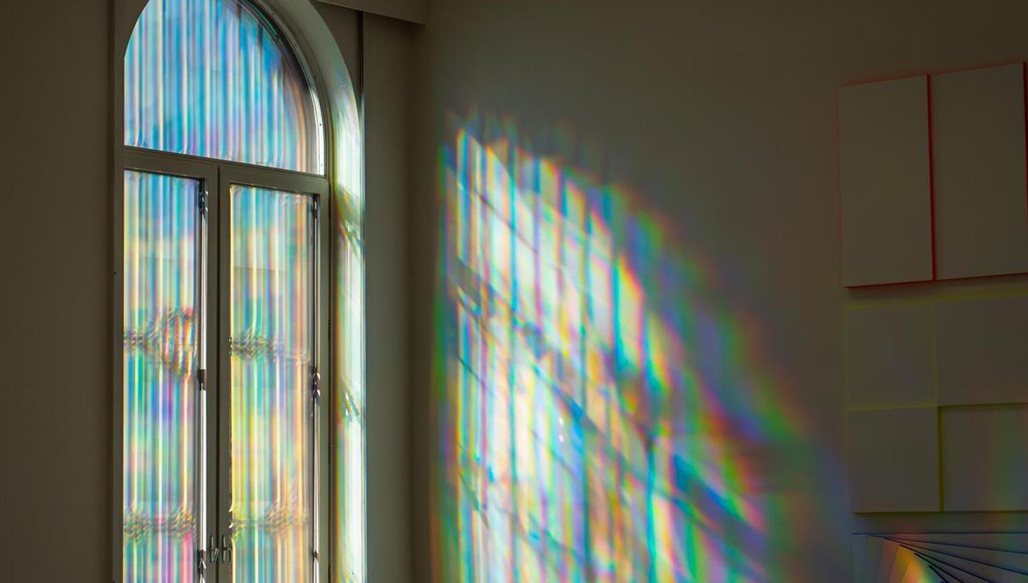 Rainbow‑colored light patterns projected on a wall and around a window.