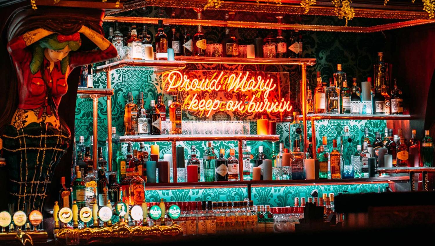 Colourful bar counter with shelved bottles behind it and a neon sign