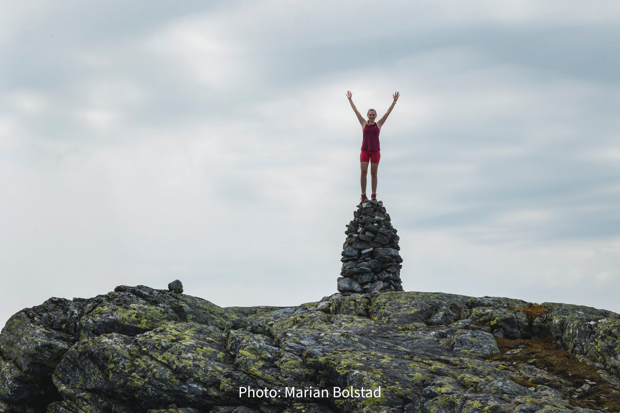 Person standing on a stone cairn in Hardanger, Norway, celebrating achievement in the mountains
