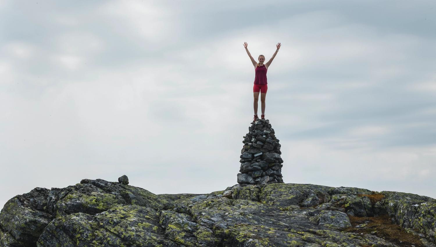 Person standing on a stone cairn in Hardanger, Norway, celebrating achievement in the mountains