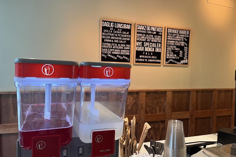 Close-up of counter with iced tea and lemonade machine, plastic glasses, cutlery and menu sign on the wall