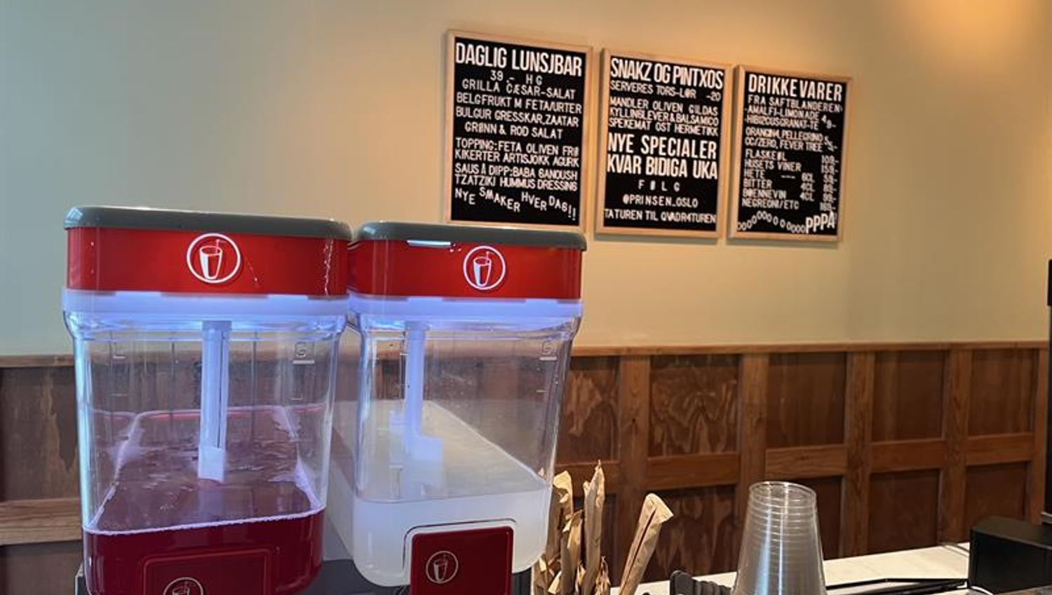 Close-up of counter with iced tea and lemonade machine, plastic glasses, cutlery and menu sign on the wall
