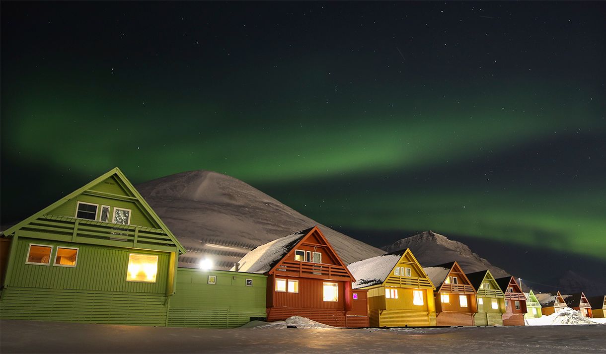 Fargerike hus i Longyearbyen med snødekte fjell og nordlys på himmelen i bakgrunnen