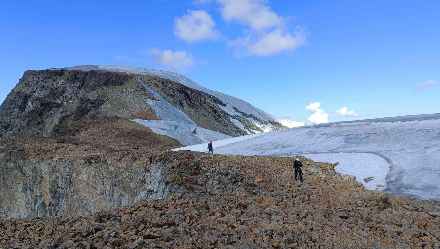 Two persons hiking up the back of a mountain.