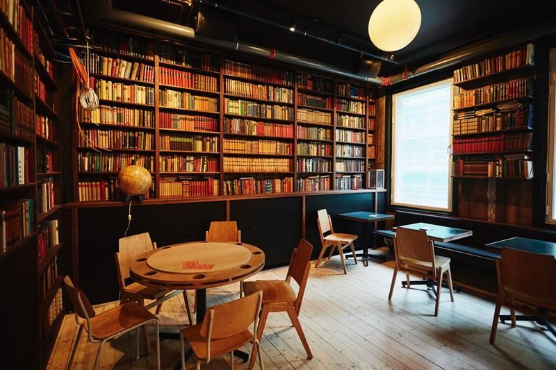 Bookcases, small tables with chairs and a high ceiling.