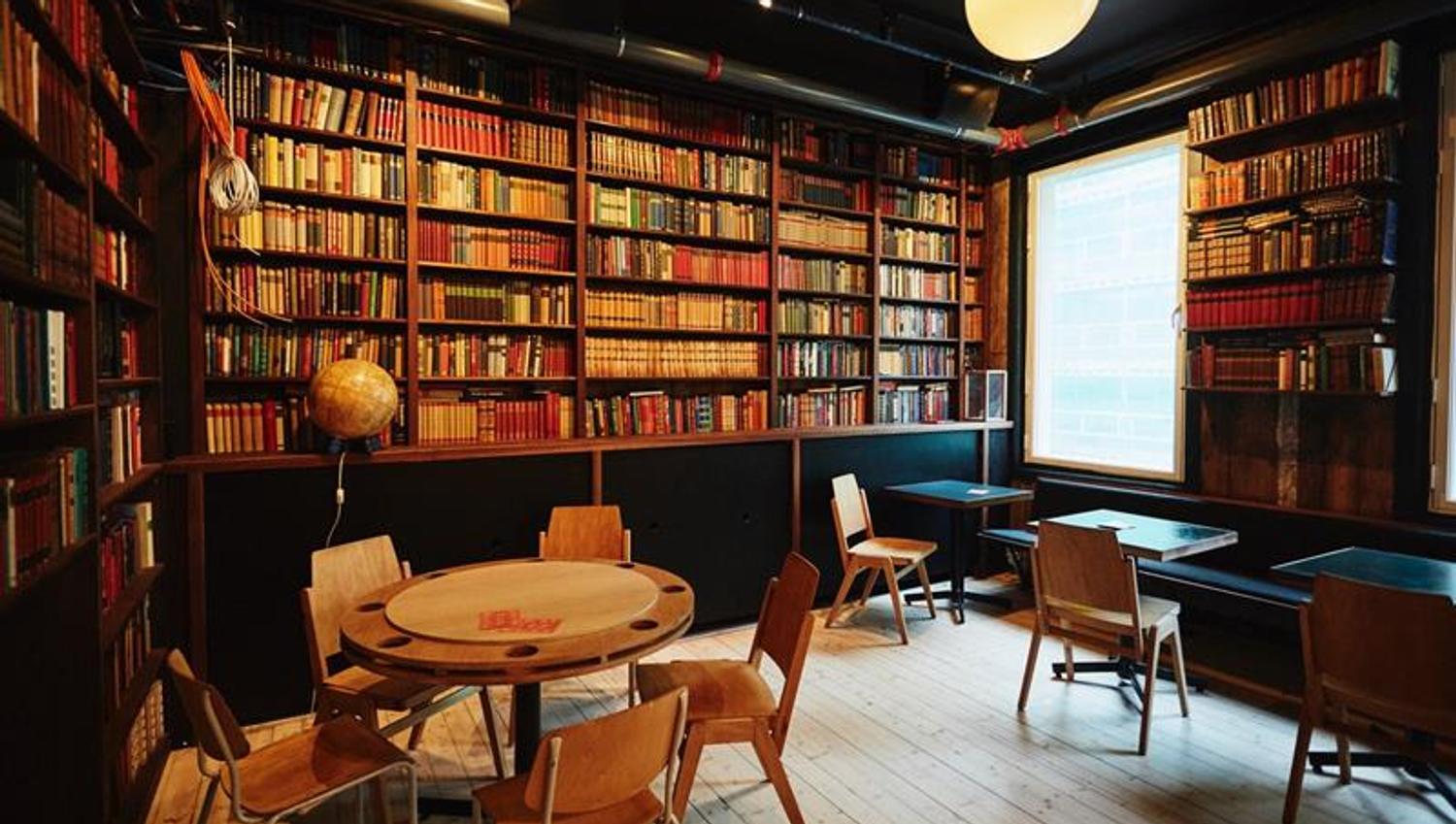 Bookcases, small tables with chairs and a high ceiling.