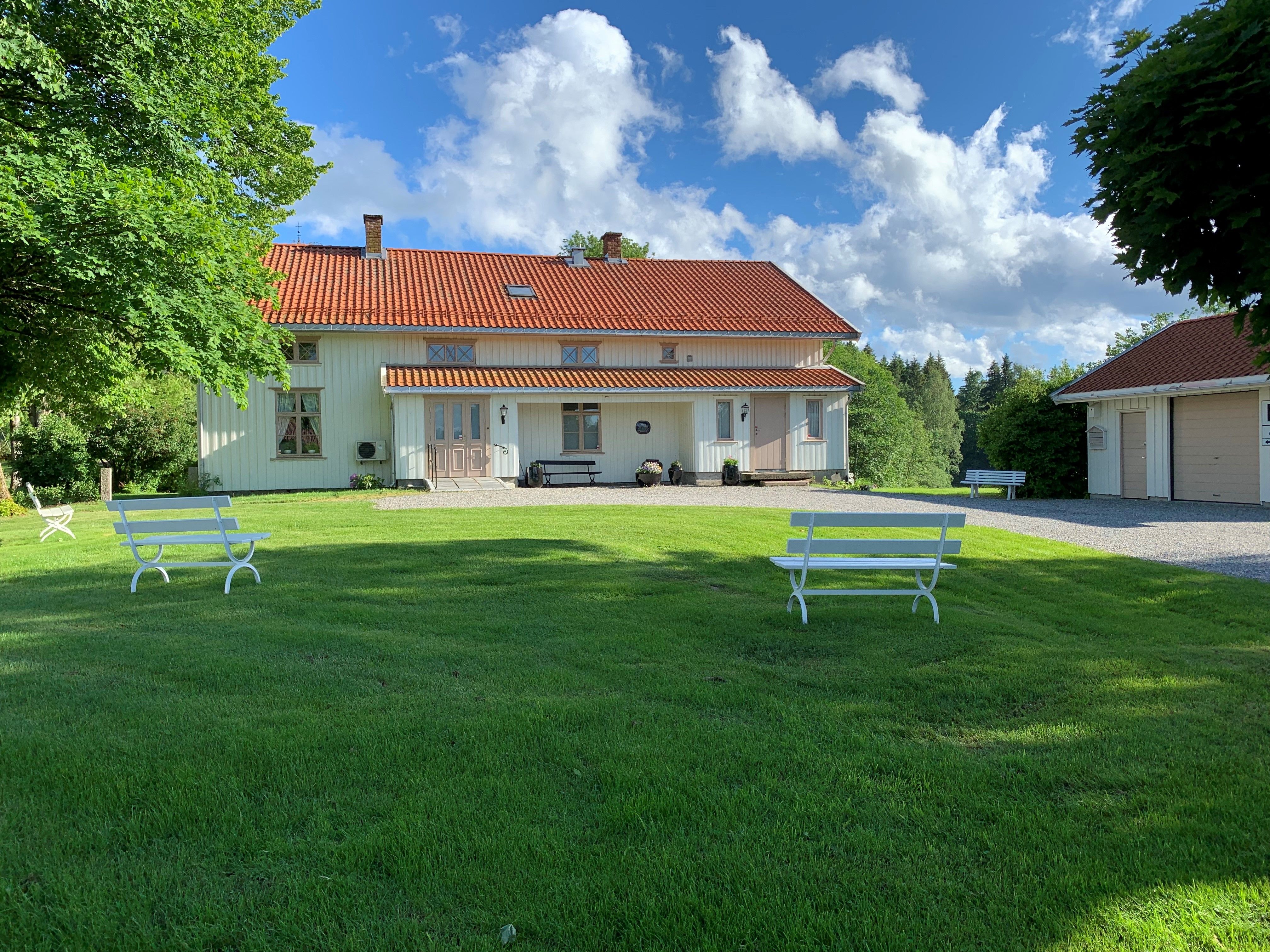 Bild av det lange hvite bygget med hagen og to benker i den.