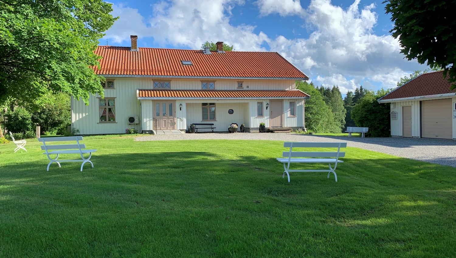 Bild av det lange hvite bygget med hagen og to benker i den.