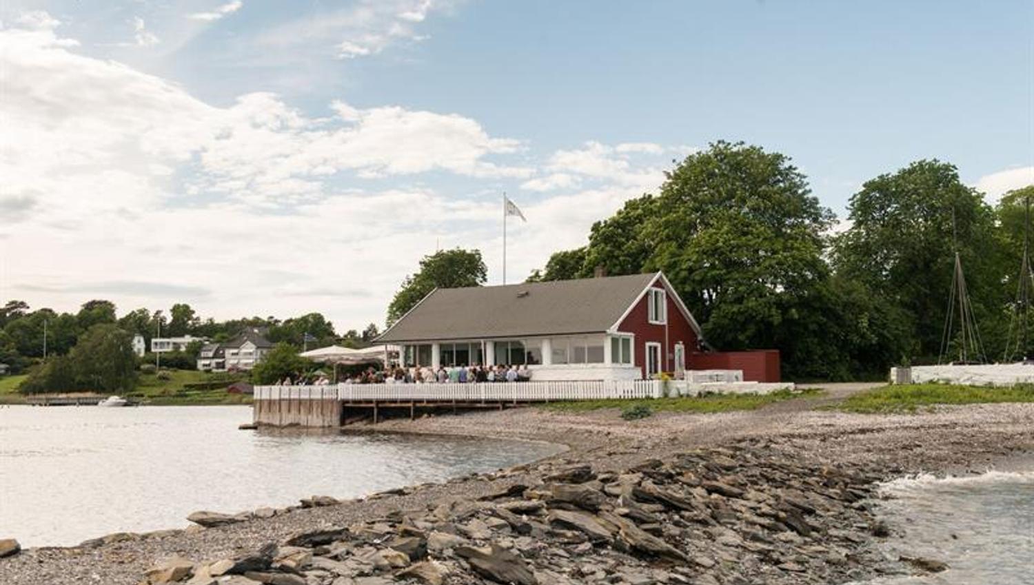 Small, red wooden house with an outdoor terrace by the beach.