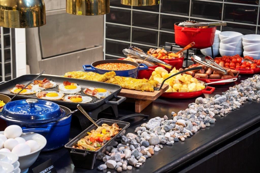Breakfast buffet with eggs, bacon, beans, potatoes, sausages, and vegetables.