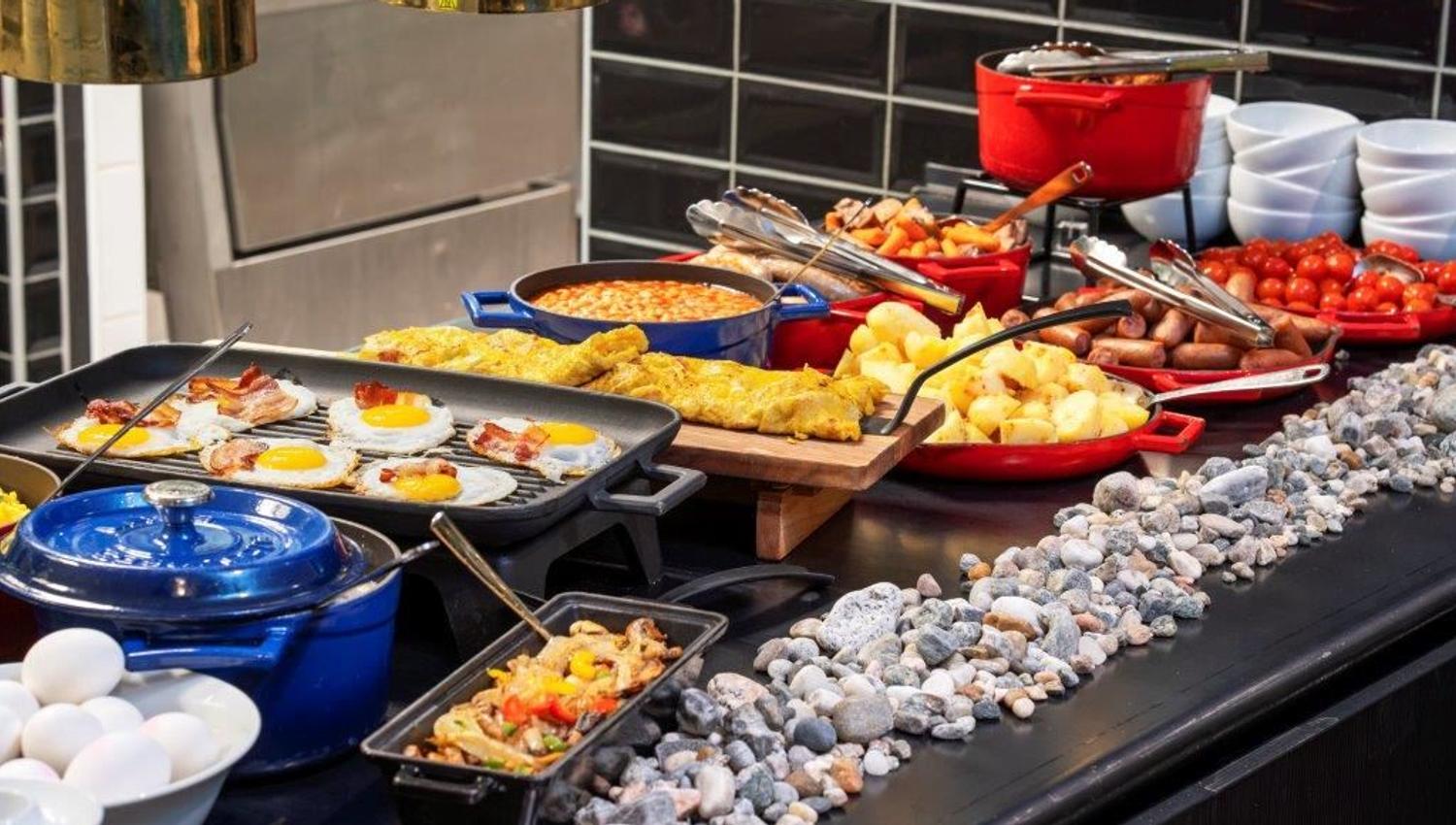 Breakfast buffet with eggs, bacon, beans, potatoes, sausages, and vegetables.