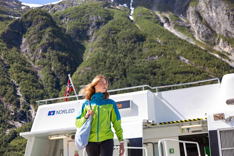 Passasjer går av Norled-båten med store fjell tett innpå under fjordcruise i Hardanger.