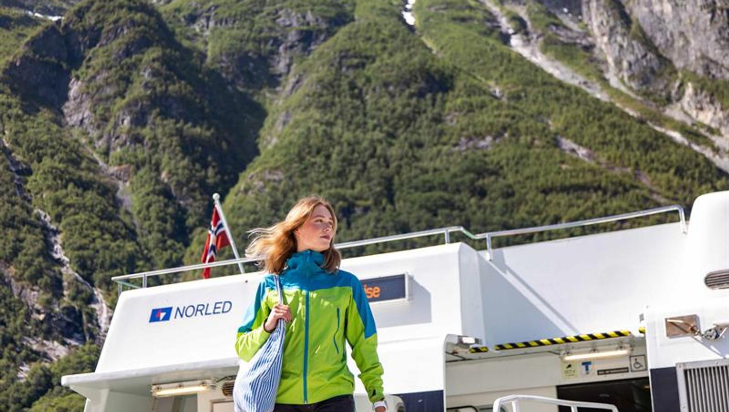 Passasjer går av Norled-båten med store fjell tett innpå under fjordcruise i Hardanger.