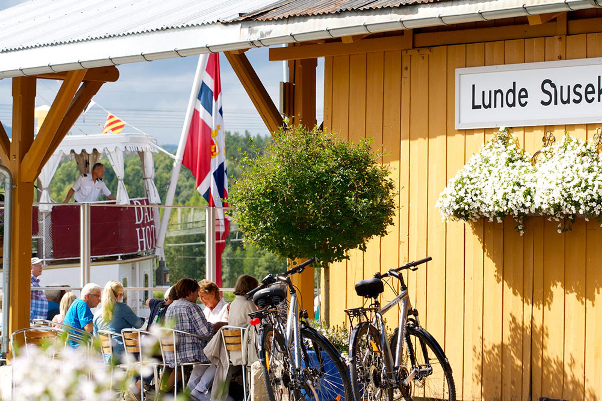 people sitting and eating at Lunde Slusekro while the canal boat MS Henrik Ibsen sails by 