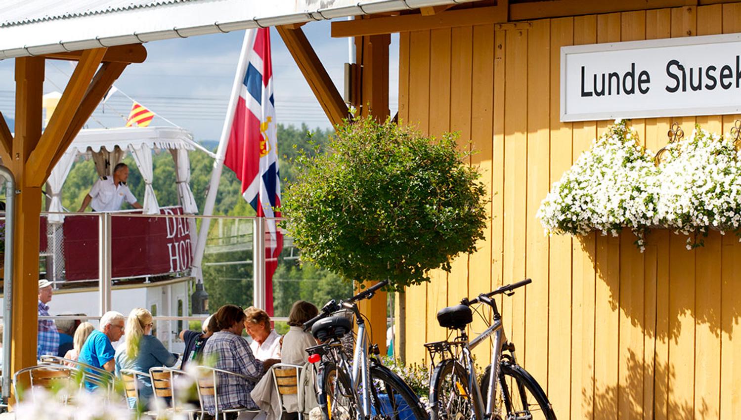 people sitting and eating at Lunde Slusekro while the canal boat MS Henrik Ibsen sails by