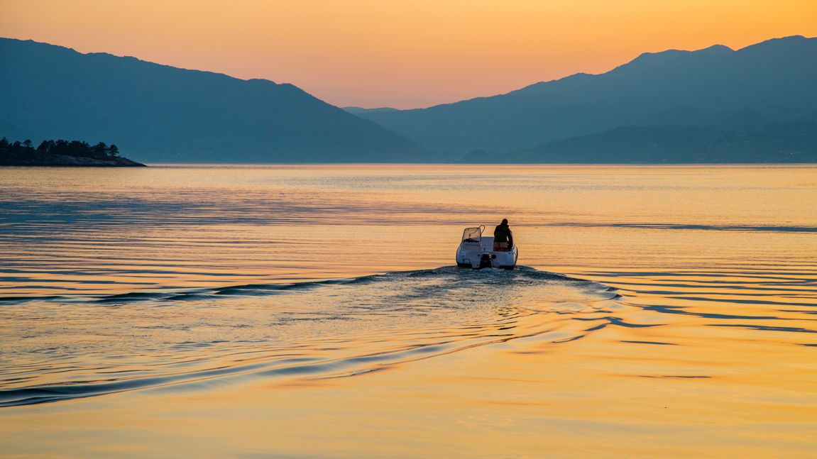 A small boat on the Hardangerfjord at sunset, with warm colors and peaceful atmosphere.