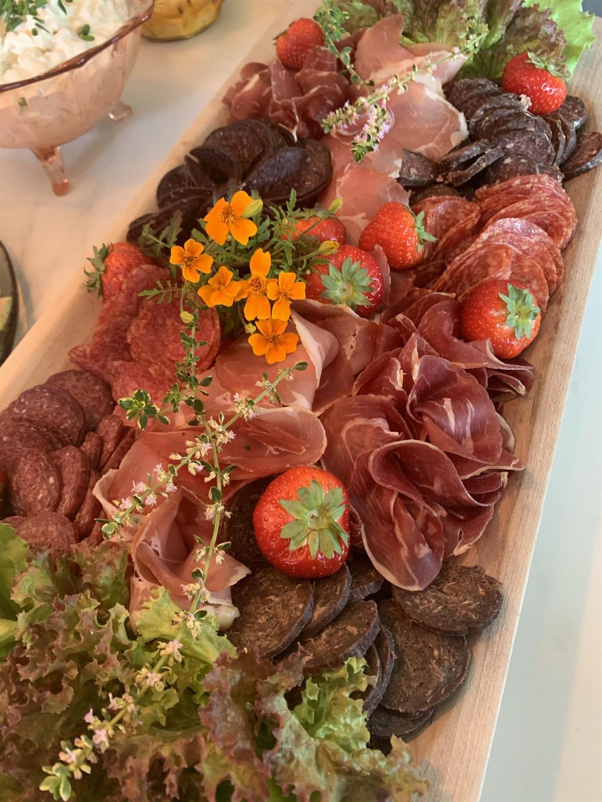  A large serving platter filled with assorted cured meats, vegetables, and decorative herbs.