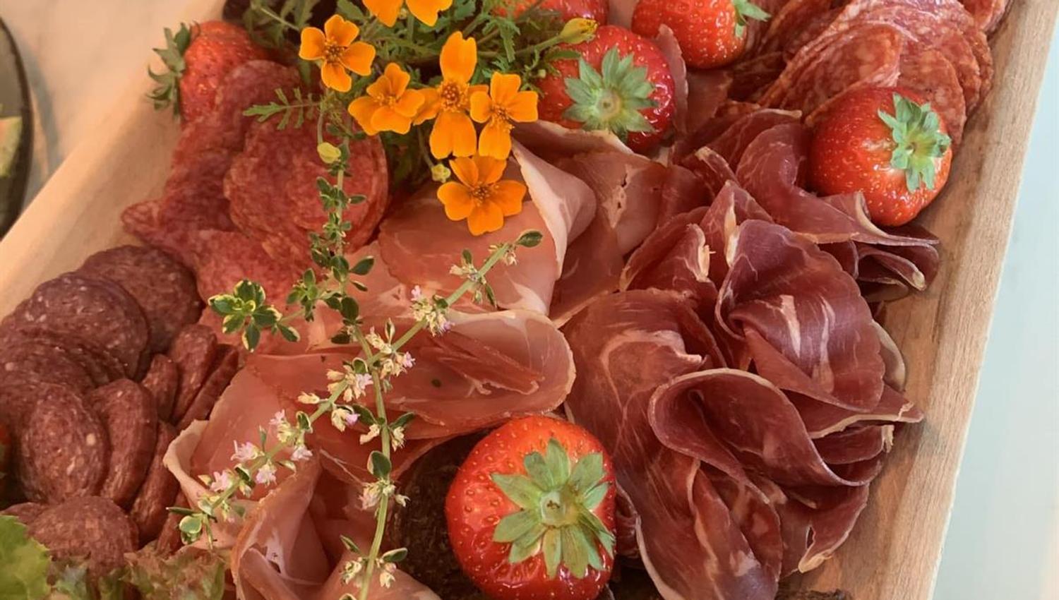 A large serving platter filled with assorted cured meats, vegetables, and decorative herbs.