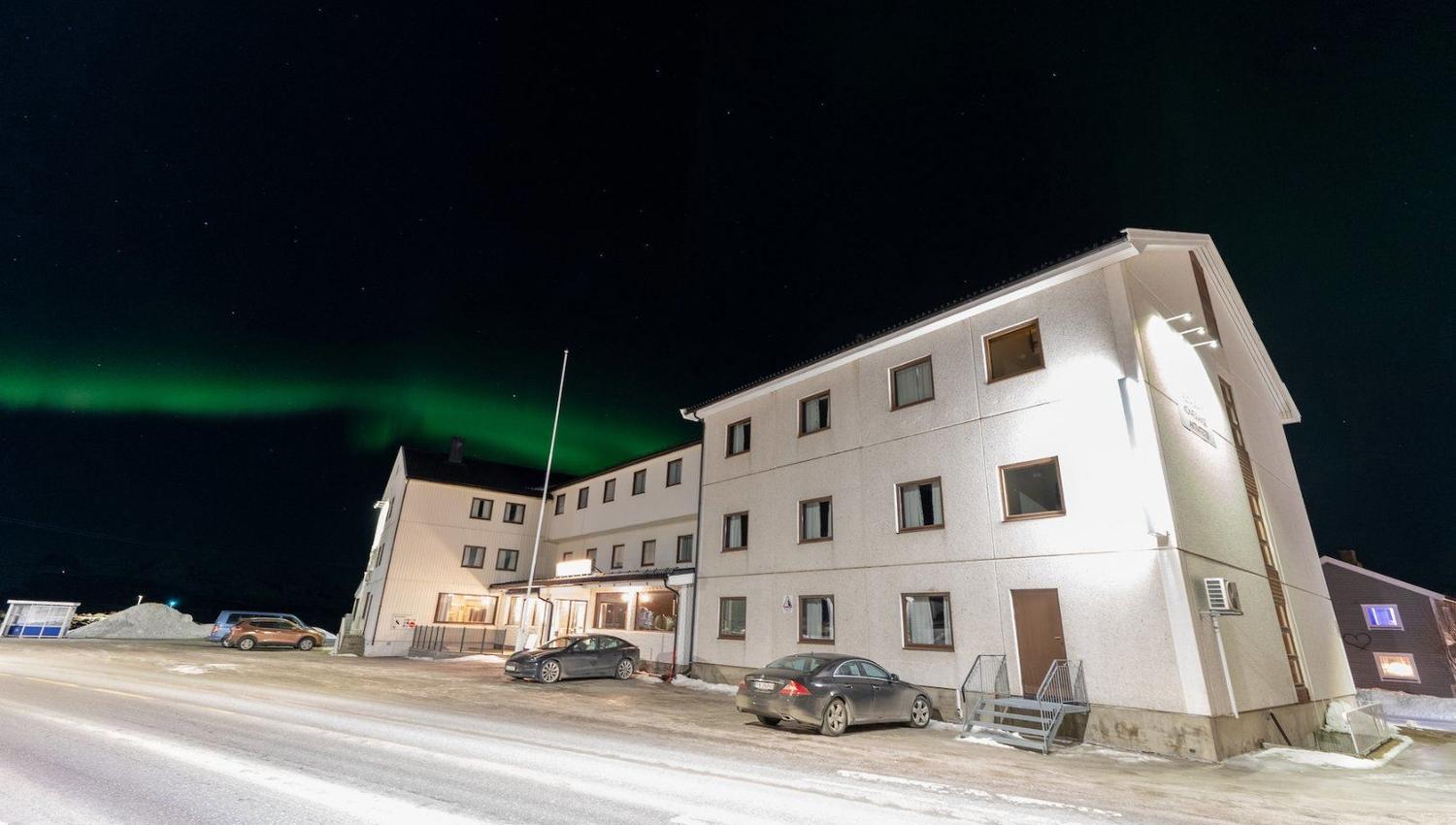 Den hvite fasaden til Reisafjord Hotel, nordlyset på himmelen