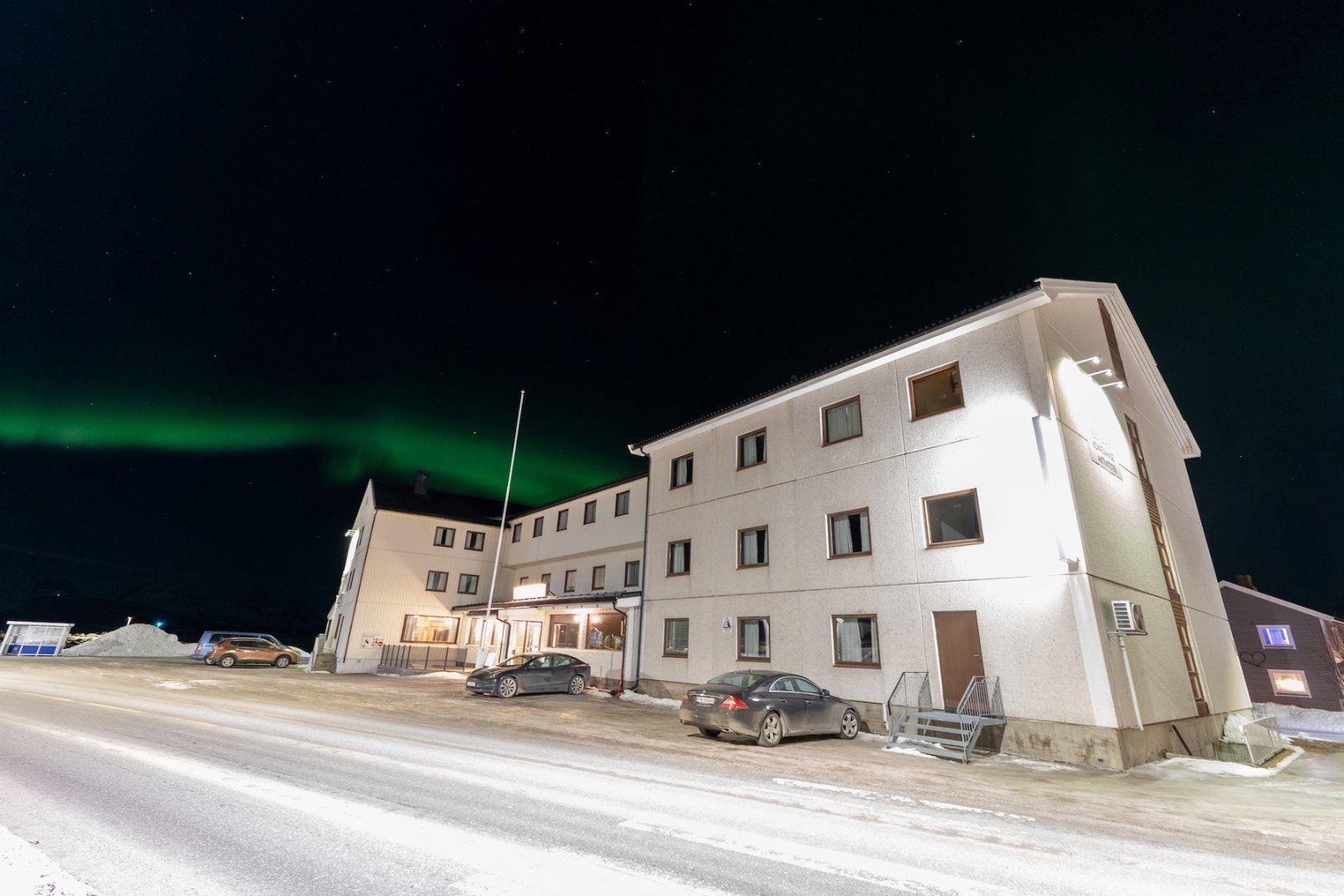 Den hvite fasaden til Reisafjord Hotel, nordlyset på himmelen