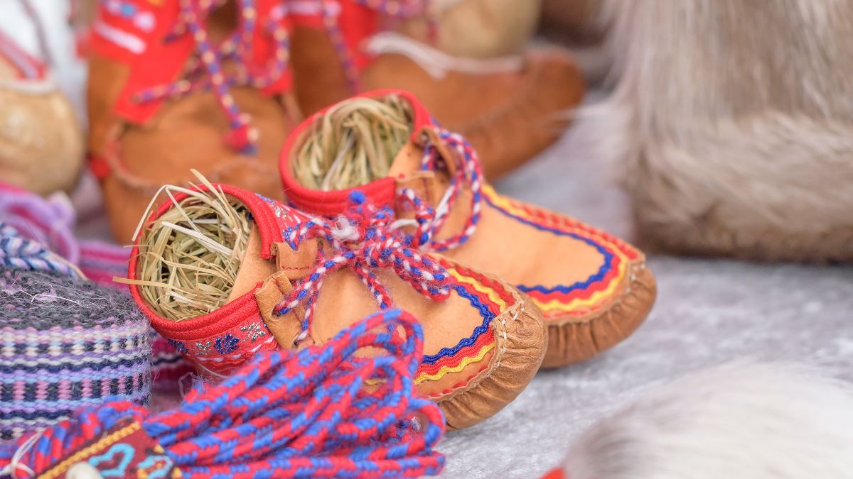 Small handmade shoes with colourful details displayed alongside traditional Sámi handicrafts.