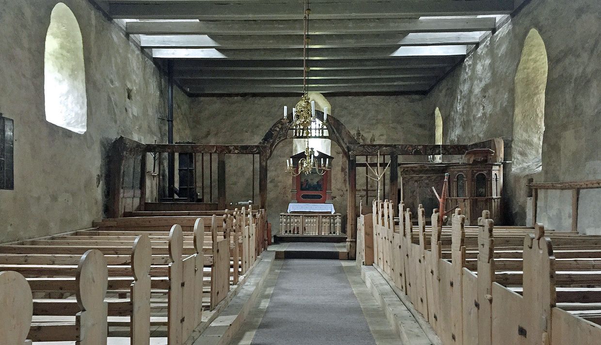 Inside the church. Old wooden church benches, white stained rock walls, the alter, a chandelair hanging from the ceiling.
