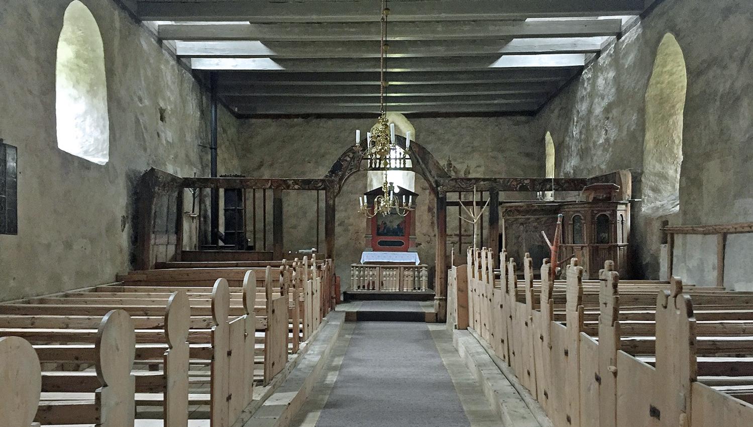 Inside the church. Old wooden church benches, white stained rock walls, the alter, a chandelair hanging from the ceiling.