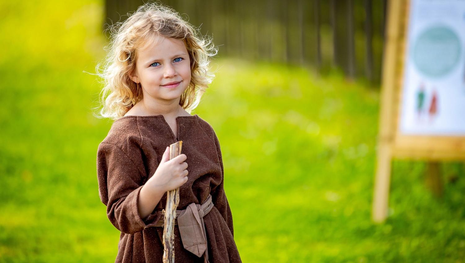 A girl with a walking stick, dressed in older clothes