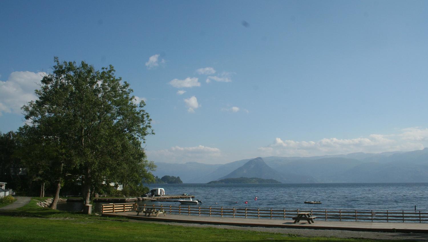 View from Hardanger Feriesenter towards the fjord with picnic benches, pier and surrounding mountains.