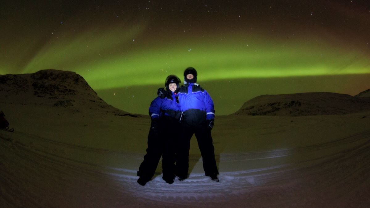 Two people standing under the northern lights