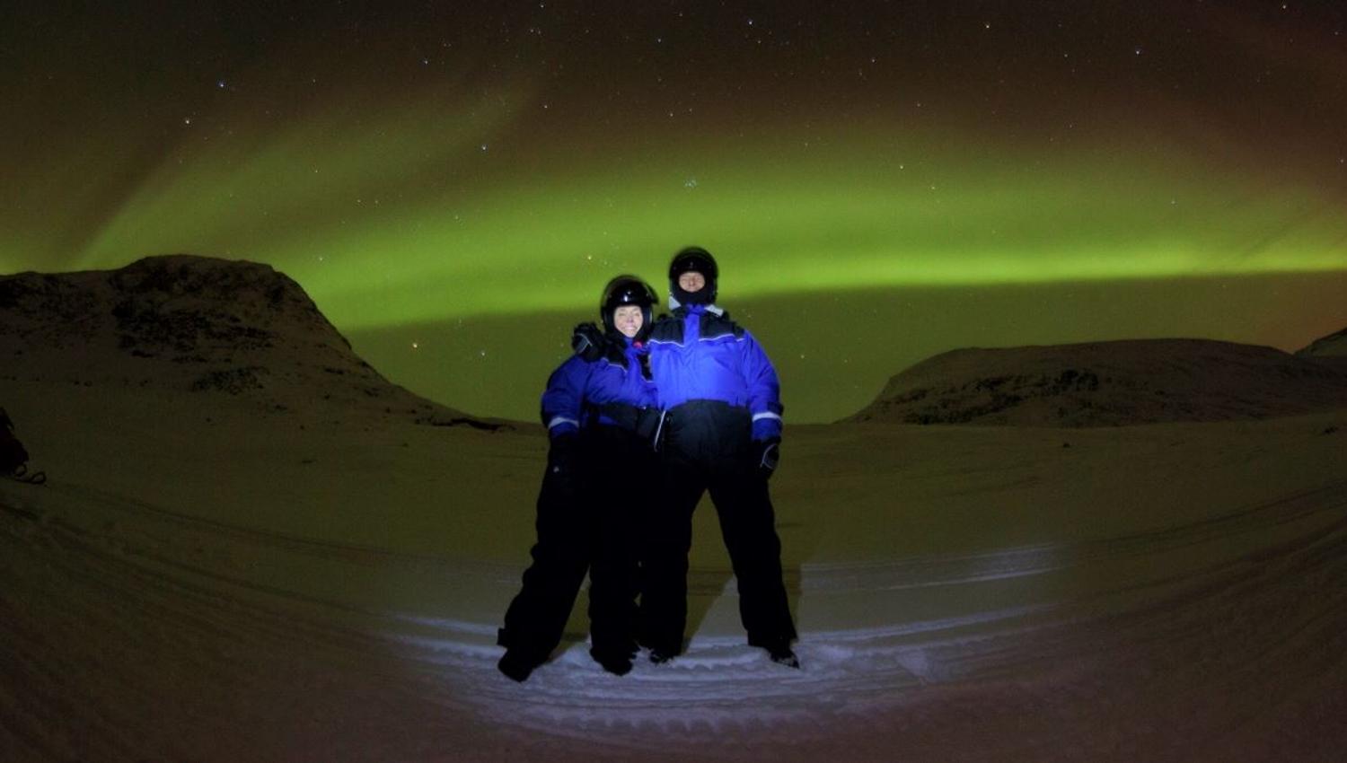 Two people standing under the northern lights