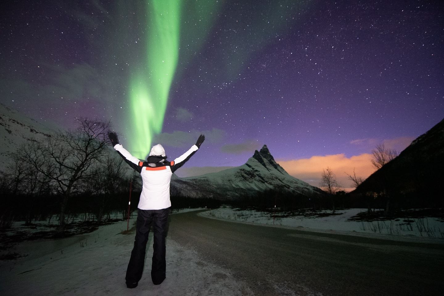 Guest poses in a white jacket before the Northern Lights and the Otertind mountain