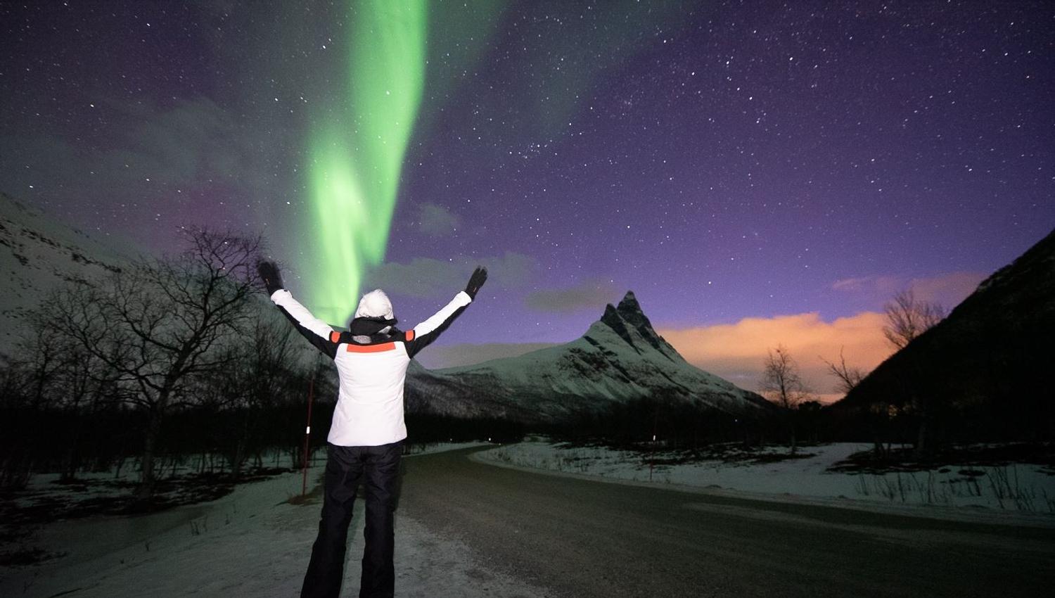 Guest poses in a white jacket before the Northern Lights and the Otertind mountain