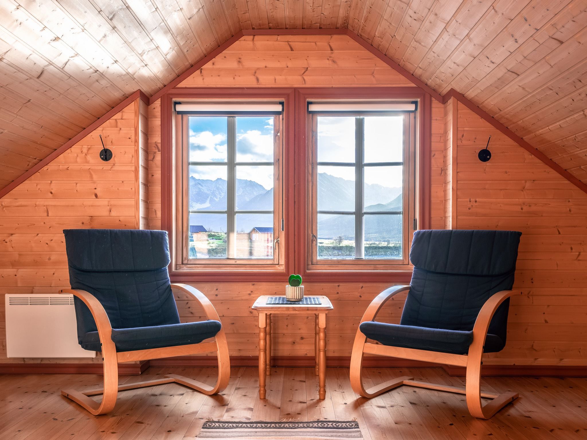 Attic lounge with two armchairs, a wooden table, and views of mountains and houses through large windows