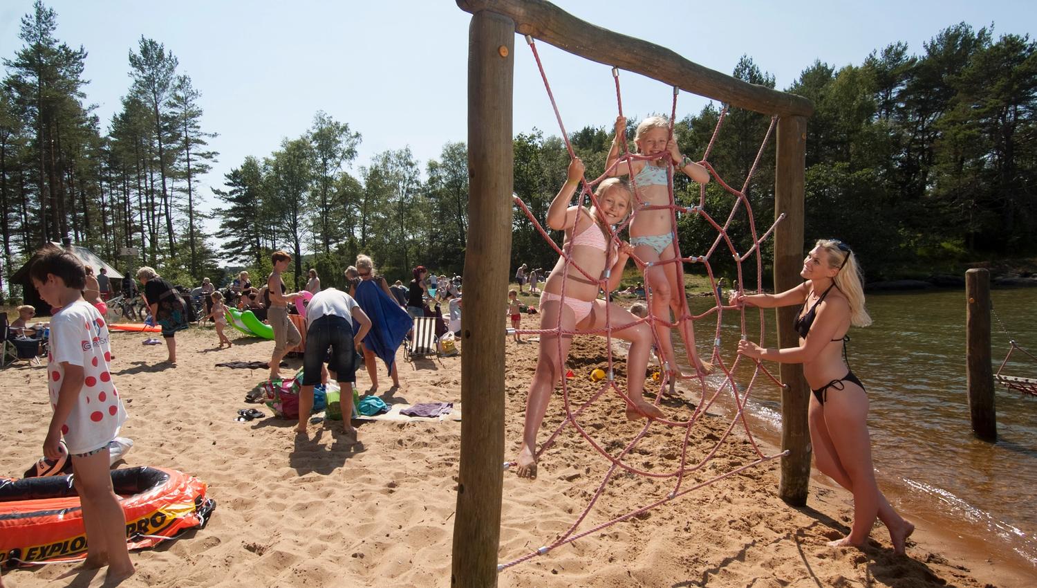 Mange mennesker på en strand, to jenter leker i en nettingvegg